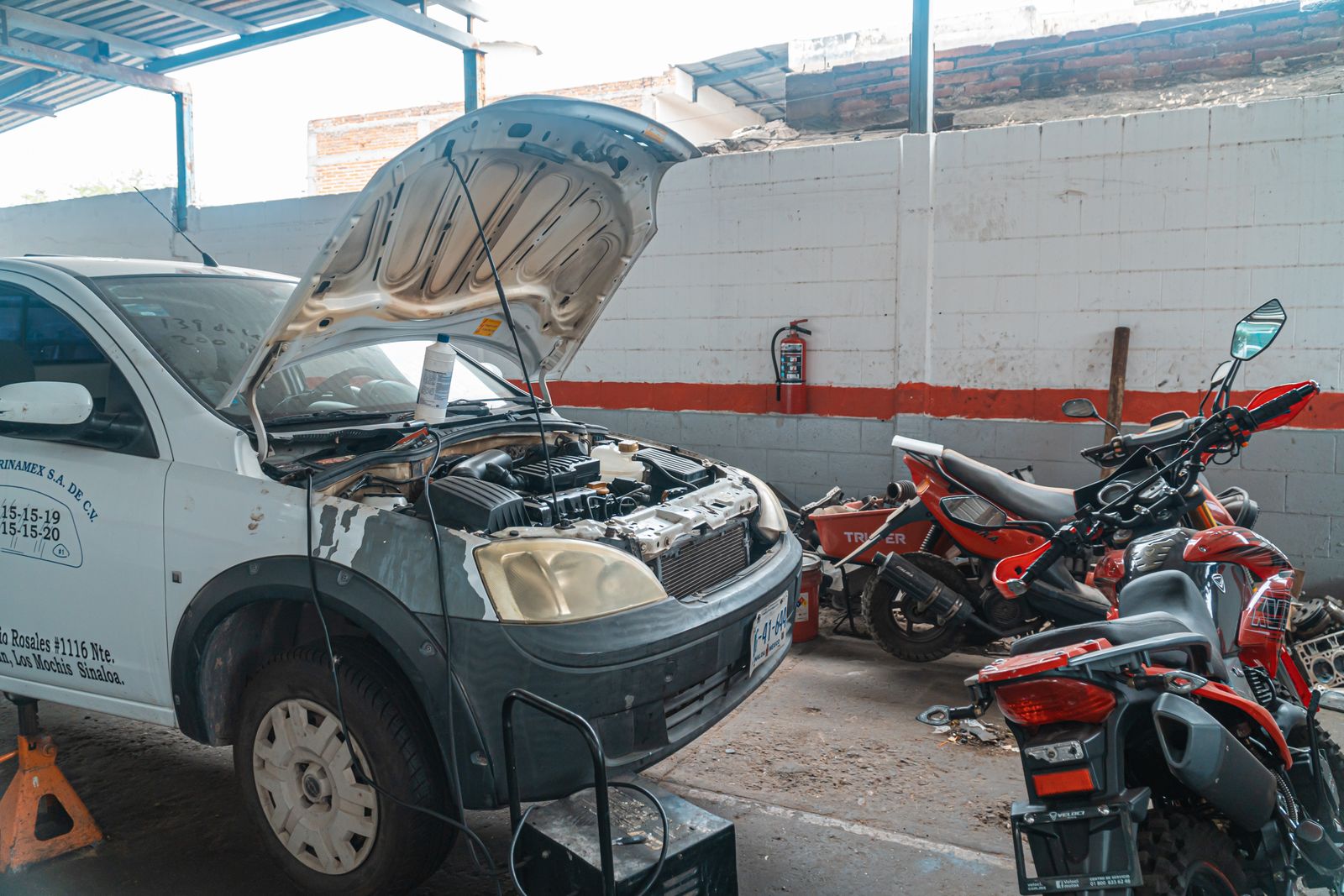 Carro sendo consertado em uma garagem com motocicletas e ferramentas ao redor.